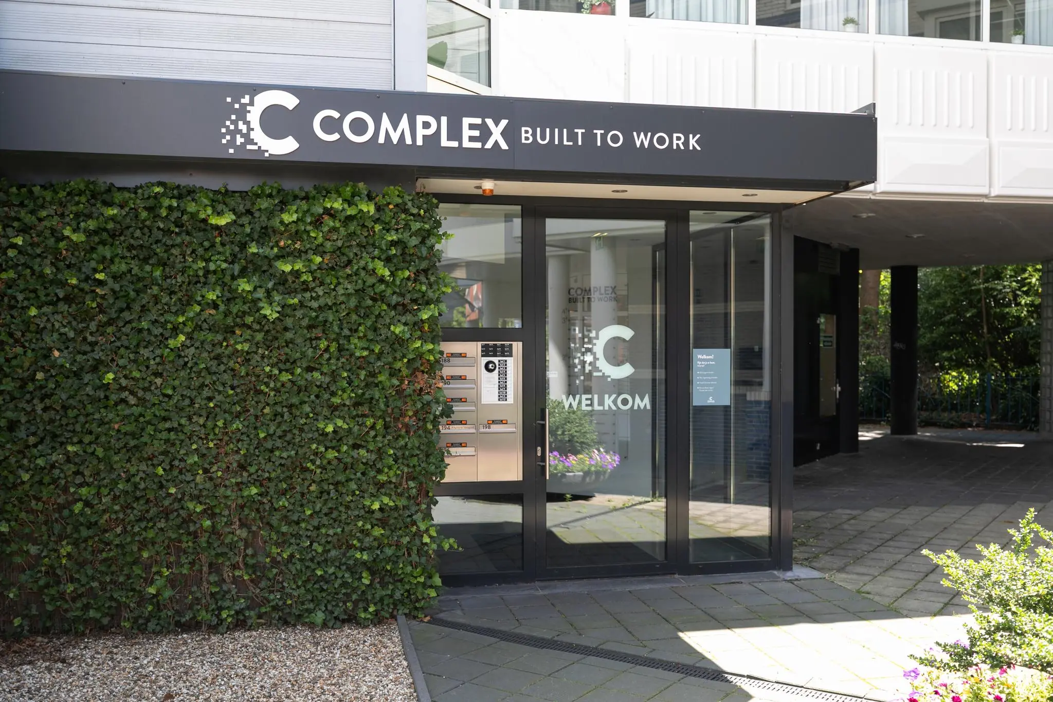 Ingang van het kantoorgebouw Complex Built to Work aan de 1e Hogeweg met glazen deuren en begroeiing aan de gevel.